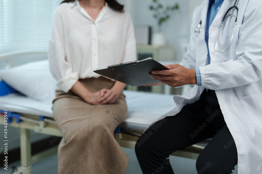 Obraz premium Doctor holding clipboard sitting next to patient on hospital bed