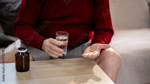 An elderly man is sitting and taking medicine in his home.
