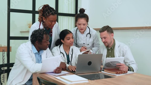 Diverse healthcare team reviewing medical information, working together on laptop and discussing patient data in modern clinical setting