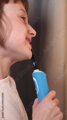 Young girl carefully cleans teeth with electric toothbrush at home in bright morning light while maintaining healthy dental routine.
