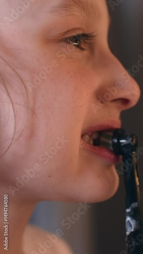 Close-up of a girl brushing teeth with an electric toothbrush in warm evening light, focused on her oral hygiene and daily self-care routine