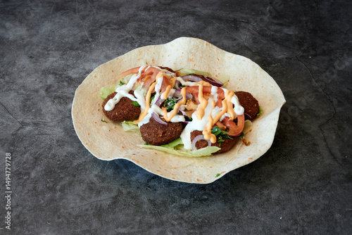 A plate of food with a tortilla wrap and a sauce. The food is made of meatballs and vegetables