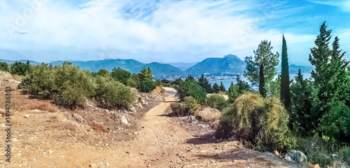 Dirt path winds through the greenery of a hilly landscape near Alanya, Turkey, offering a scenic view of Mediterranean Sea and distant mountains. Peaceful setting creates a perfect hiking experience