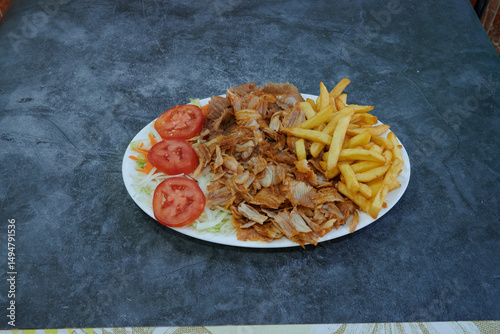 A plate of meat and fries with a side of tomatoes and lettuce. The plate is white and the food is brown