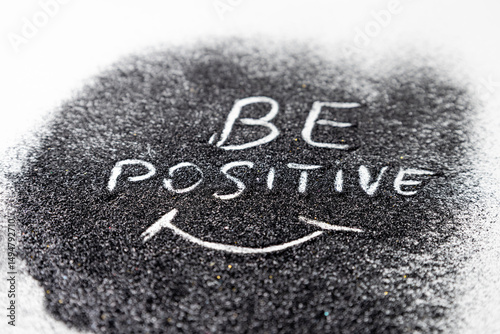 On the black glitters drawing words BE POSITIVE and the smile white background. Abstract minimalist composition from glitter