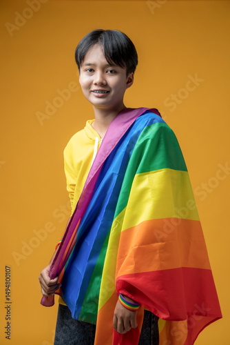 Portrait of Asian teenage girl with rainbow lgbtq flag on shoulder against yellow color background in studio, tomboy