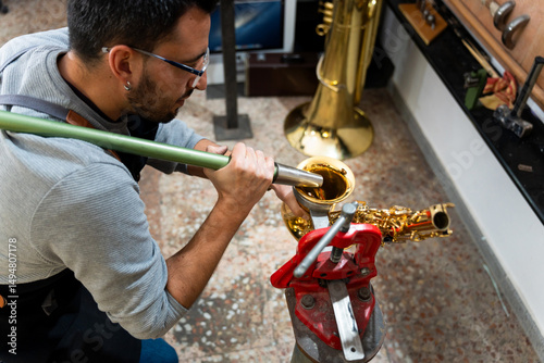 Instrument repairman cleaning saxophone with vacuum cleaner in workshop