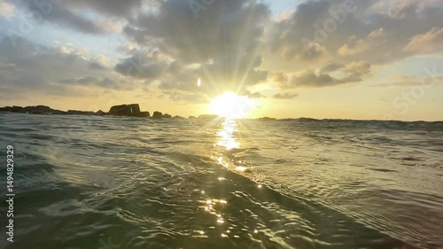 Captivating image of a golden sunset peeking over ocean waves, captured at sea level. The sun's rays create a serene and peaceful atmosphere over the calm water surface