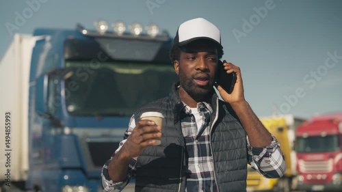 Wallpaper Mural Serious African American male wearing cap and warm vest while talking on smartphone near parked trucks. Holding takeaway coffee while explaining situation or discussing schedule. Communicating. Torontodigital.ca
