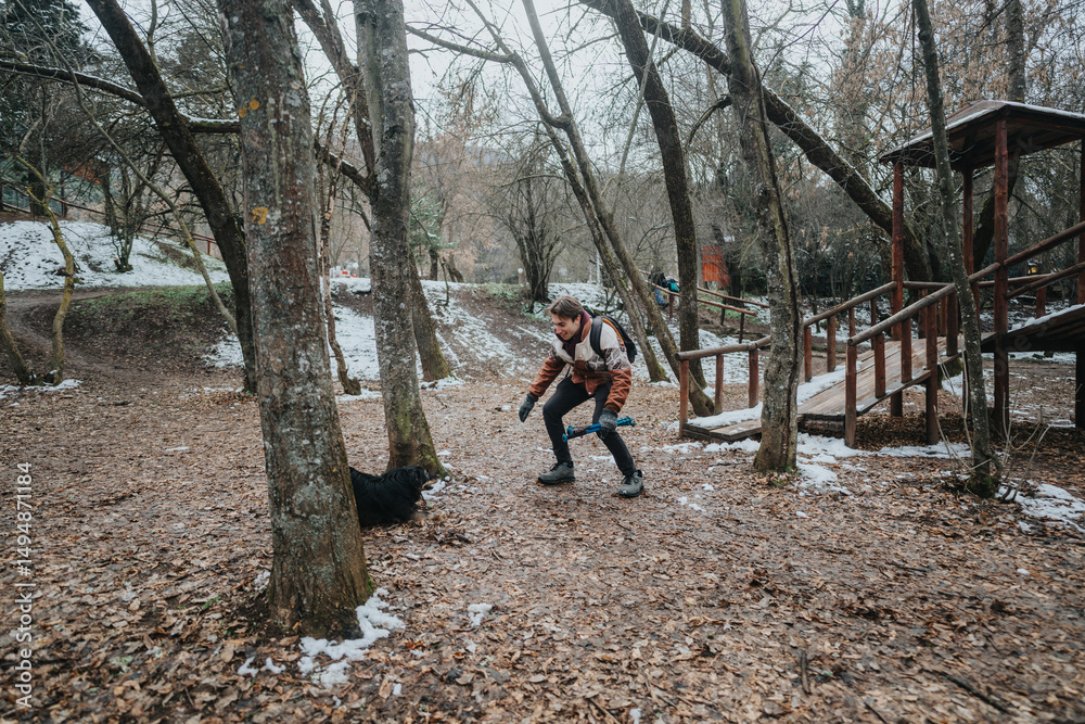 Fototapeta premium A person playing with a dog in a forest during a cold winter day, showcasing friendship and outdoor enjoyment in a natural setting.