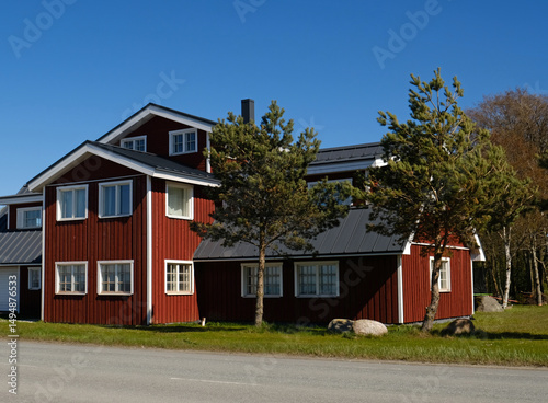 Traditional red wooden house with white trim near Baltic Sea coast. Pine trees and blue sky. Nordic architecture and serene coastal living. Perfect for themes of contemporary living and real estate.