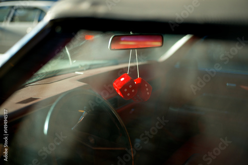 Red fuzzy dice hang from the rear-view mirror of a vintage car, sunlight dapples the interior. New York City, USA