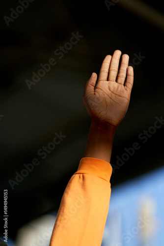 Raised hand of a colored person in a gesture of participation against a blurred background.