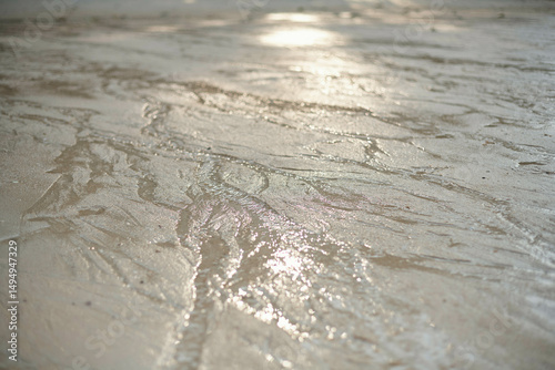 Wet sand with intricate patterns created by receding water reflecting sunlight. Thailand photo