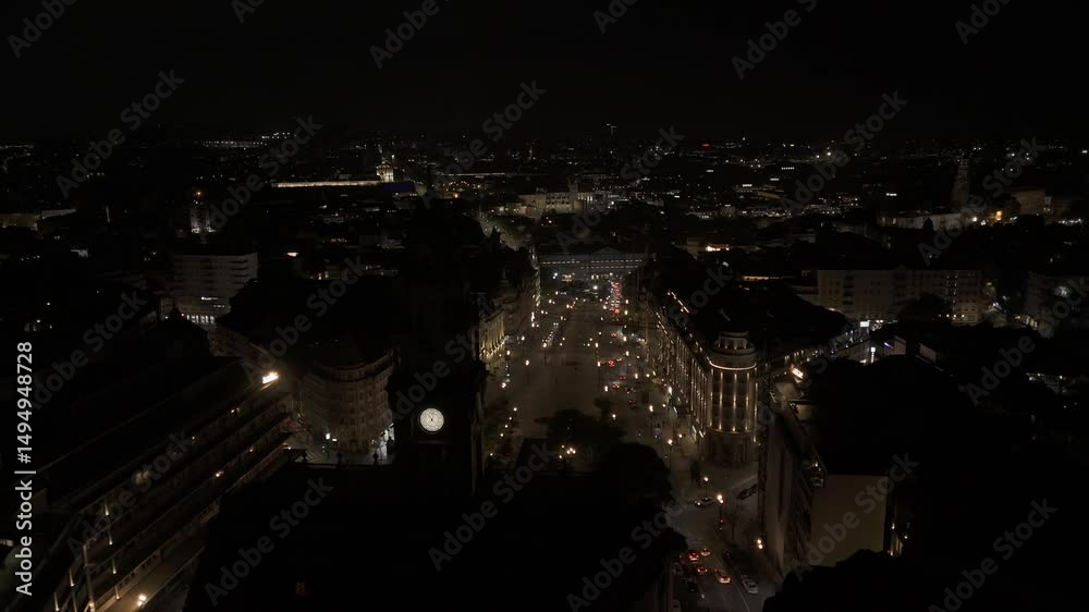 Drone flies backwards from Aliados Square at night as the clock tower of city hall comes into frame in Porto, Portugal