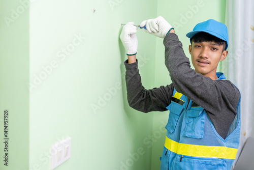 Asian male worker uses screwdriver to tighten screws on gypsum board wall.