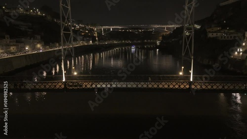 Drone hovers over Douro River in front of bottom tier of Luis I bridge at night in Porto, Portugal