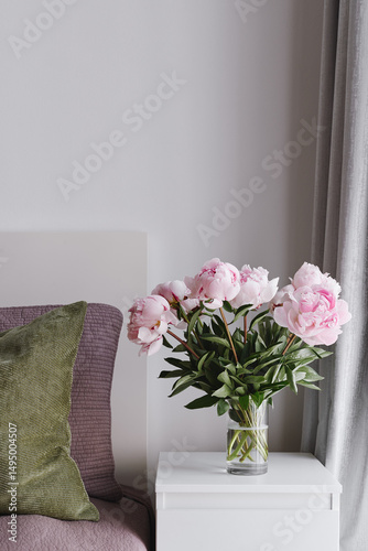 Minimal Bedroom Interior with Fresh Pink Peonies in Glass Vase. Flowers as Home Decor