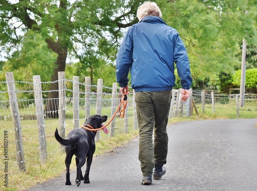 A person walking away from camera with a dog on a lead at heel.