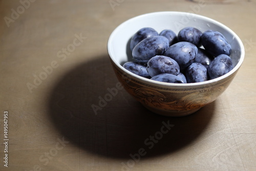 Ceramic bowl full of raw fresh blue plums.