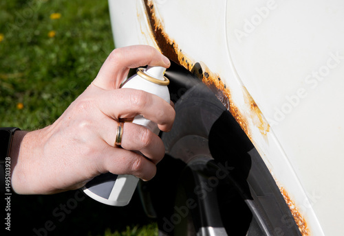 Detail view of person hand apply home use car spray rust stop converter liquid on vehicle rusty parts. 