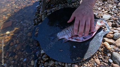 A cook cuts fish outdoors with a knife