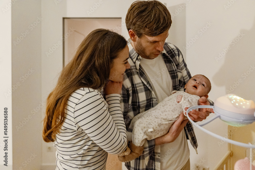 Fototapeta premium Mother stands and smiles while leaning on father's shoulder and looking at the child he is holding