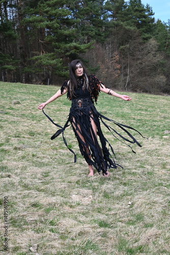 Hexe im schwarzen Kleid vor dem Wald 