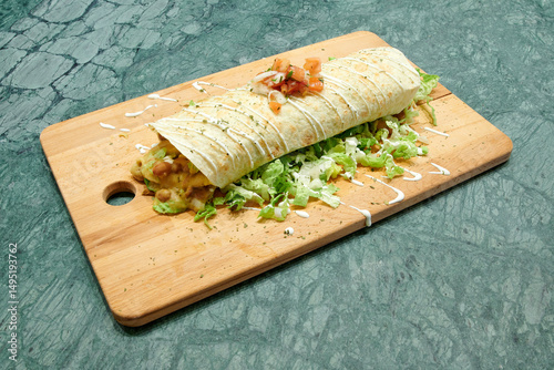 A burrito with lettuce and cheese on top of a wooden cutting board. The burrito is wrapped in a tortilla