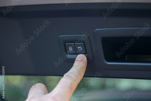 Index finger near the trunk lid closing button of a modern vehicle