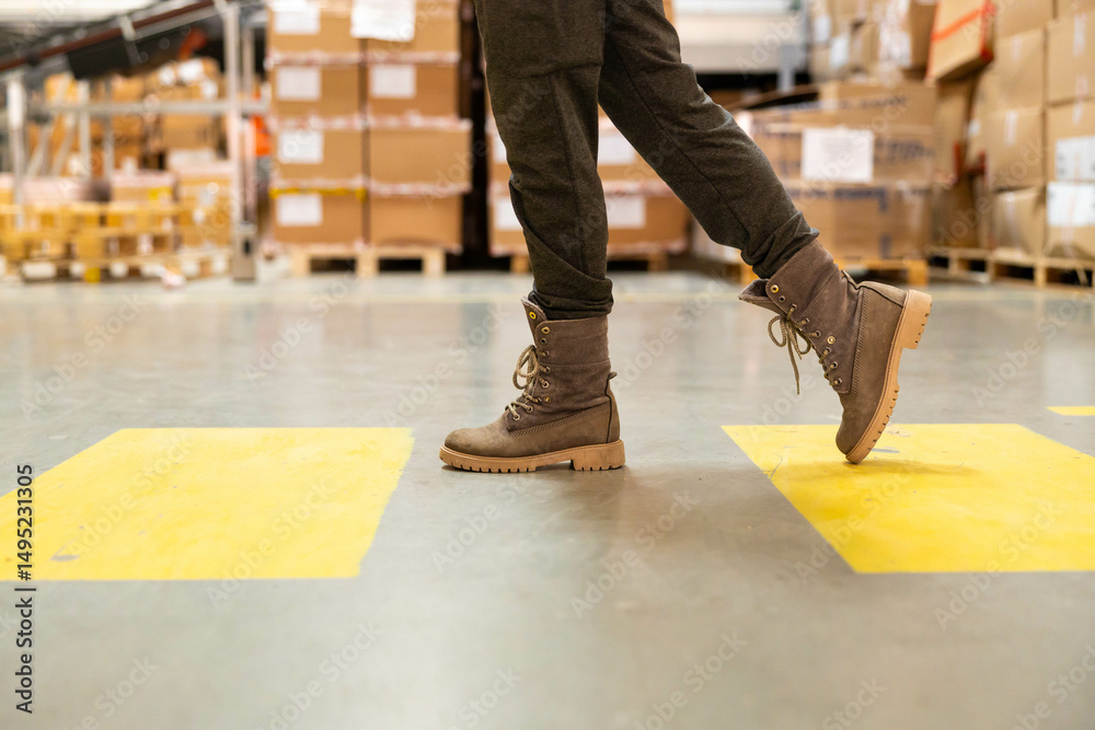 Obraz premium Close-up of the shoes of a warehouse worker walking along a marked walkway in a warehouse.using the marked pedestrian path in the warehouse.Pedestrian safety concept in a warehouse