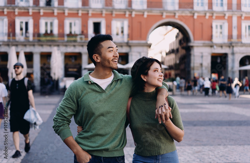 Foto Interracial couple exploring historic square arm in arm, looking around with awe