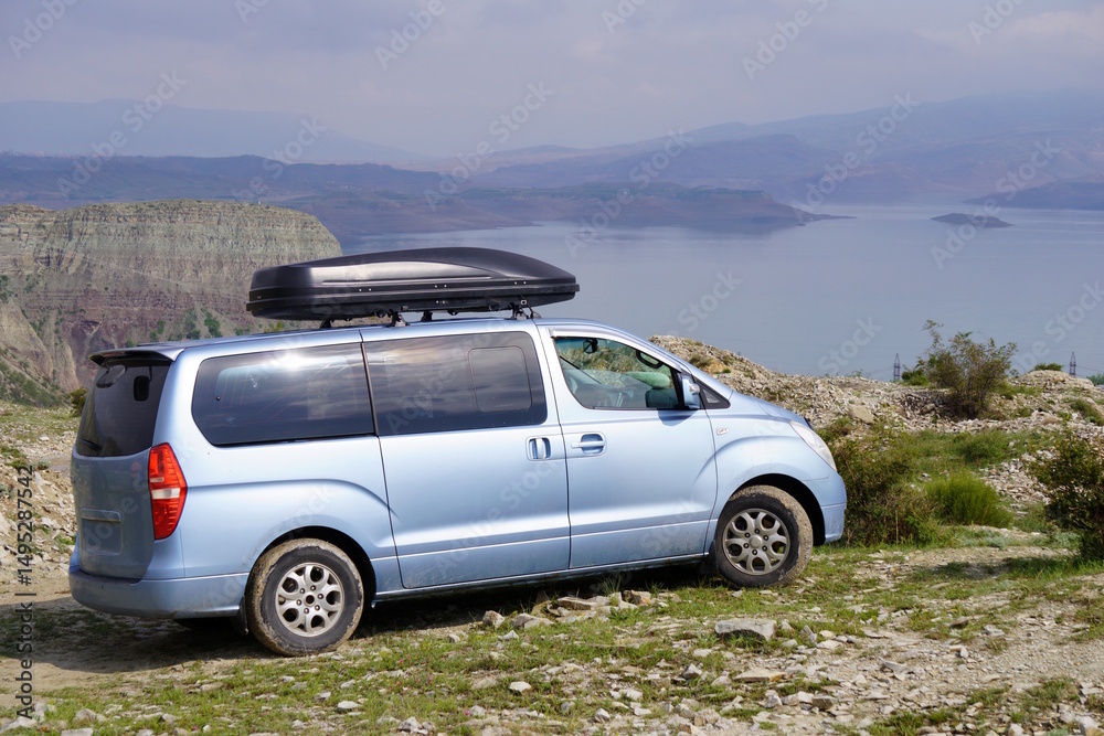 Naklejka premium A car with an upper trunk on the background of a river and mountains. Recreation and travel.