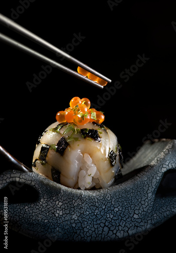 Refined sushi sphere topped with salmon roe and seaweed, served in a Japanese ceramic bowl. Chopsticks delicately lifting the garnish. Gourmet concept with dark elegant background