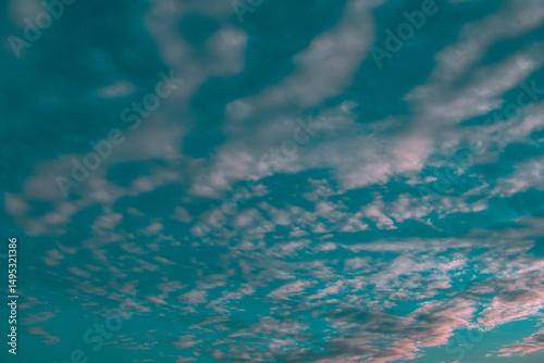 Soft, scattered clouds stretch across a vibrant teal sky, reflecting hues of pink and purple during a tranquil sunset.