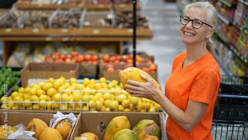 Portrait of smiling happy pretty mature woman choosing a papaya in a grocery store.