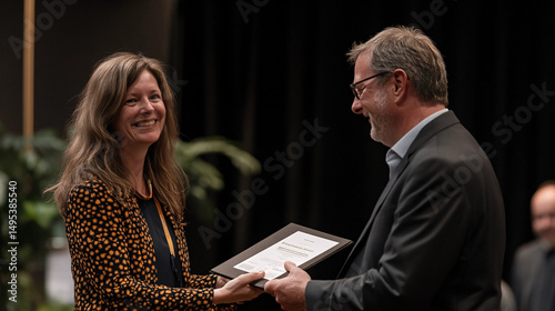 A woman happily receives a document from a man during a formal ceremony, smiling brightly.