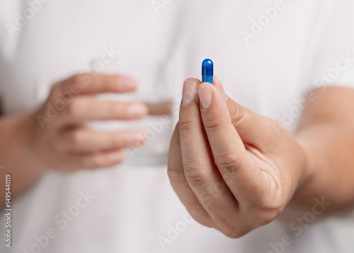 Woman in white t-shirt holding blue capsule in fingers and water glass in hand closeup