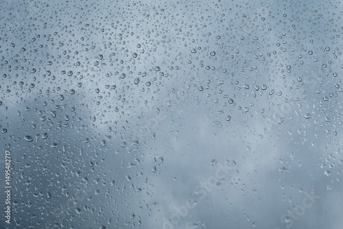 Water Drops On The Pane. Raindrops of Water On The Window Glass. Blue Cloudy Sky in a Background. Condensed Water Vapor On The Window Pane. 