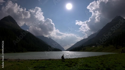 woman walks along place moulin lake shore in italian alpine valley