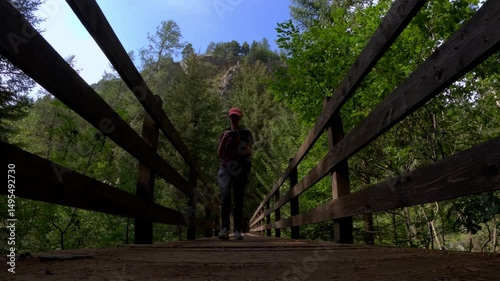 woman walks and stops to take photo on wooden bridge in Bionaz forest