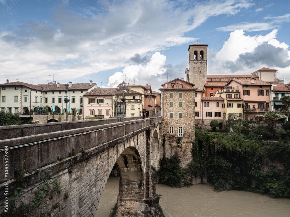 Fototapeta premium The historic Devil's Bridge crossing the Natisone River with pastel old town buildings in Cividale del Friuli, Italy.