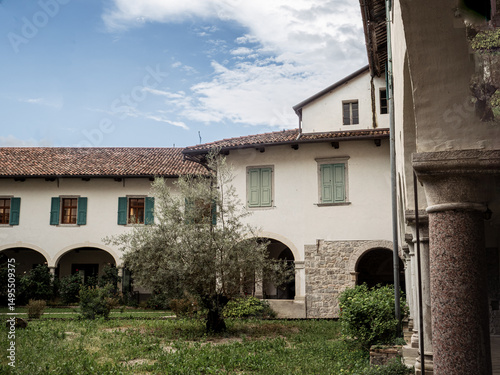 Historic courtyard with arcades, stone walls, and olive tree at the Monastero di Santa Maria in Valle in Cividale, Italy.