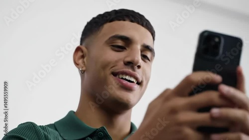 Smiling young man holds a smartphone wearing a green collared shirt indoors