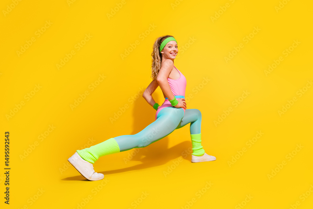 Fototapeta premium Young woman in vibrant retro activewear stretching against yellow background showing fitness and happiness