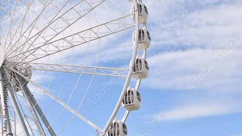 Giant ferris wheel cabins rotate smoothly against blue sky, offering panoramic views and thrilling leisure experience outdoors.