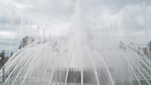 Dynamic fountain jets burst upwards, creating a mesmerizing water display against cloudy sky in city park, capturing summer urban atmosphere