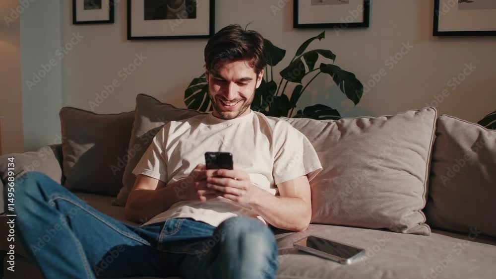 Young man using mobile phone while relaxing on sofa in living room Young man using mobile phone while relaxing on sofa in living room
