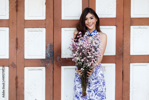 Wallpaper Mural Beautiful Asian chinese woman in traditional cheongsam smiling, posing with a large bunch of fresh spring flowers against a classic wooden door. Torontodigital.ca