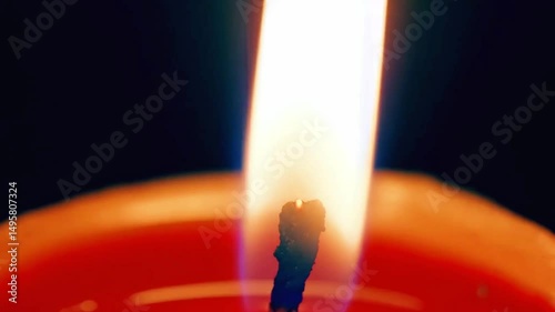 Close-up of a burning candle wick with bright flame and soft orange wax